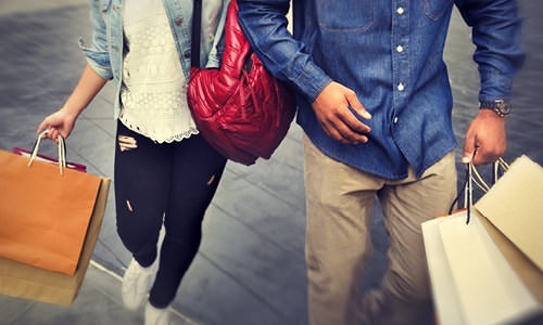 couple walks arm-in-arm down city street with shopping bags in hand